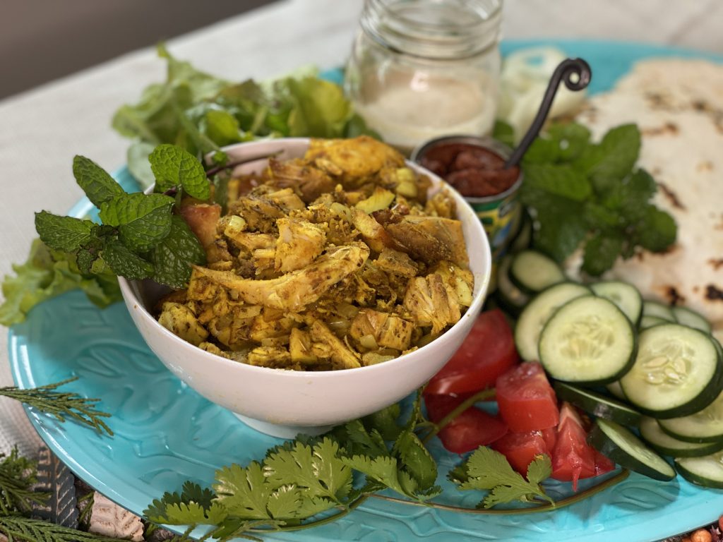 White bowl of Turkey Shawarma with flatbread, sliced vegetables, herbs and tahini