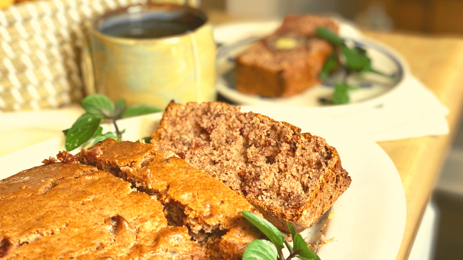 brown sliced bread on a white plate with mint. Coffee cup and basket in the background