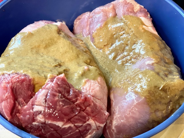 two large pieces of pork meat in a blue melamine bowl covered in a light brown liquid marinade