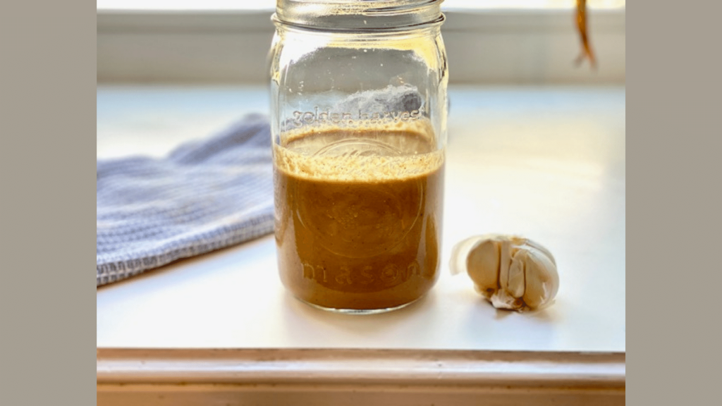 Mason Jar filled with the best basic meat marinade in a windowsill next to half a head of garlic.